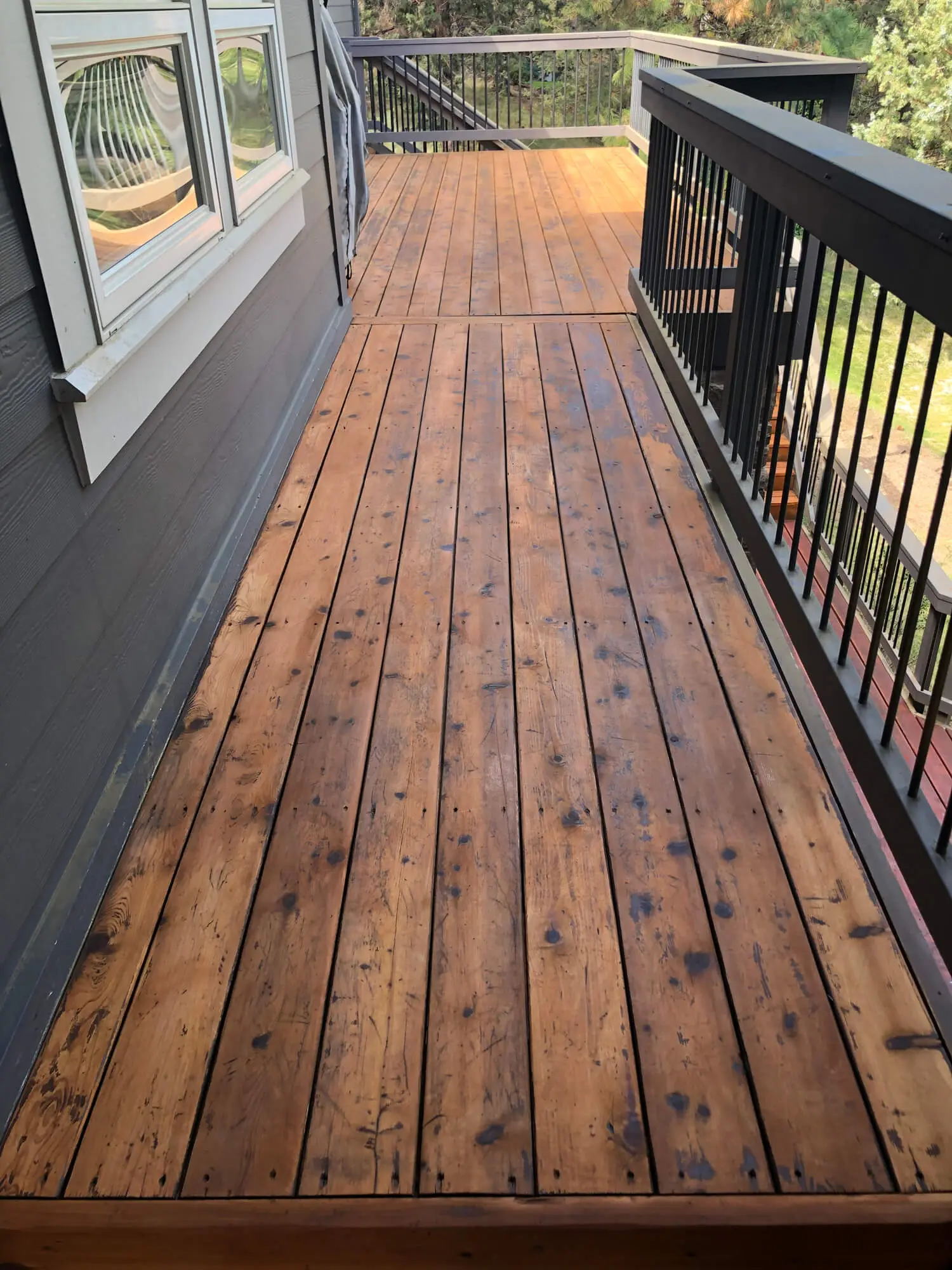 A professional exterior view of a residential backyard featuring a wooden deck with new white vinyl railings and stairs, showcasing a completed project by West Rivers Painting in Bend, OR
