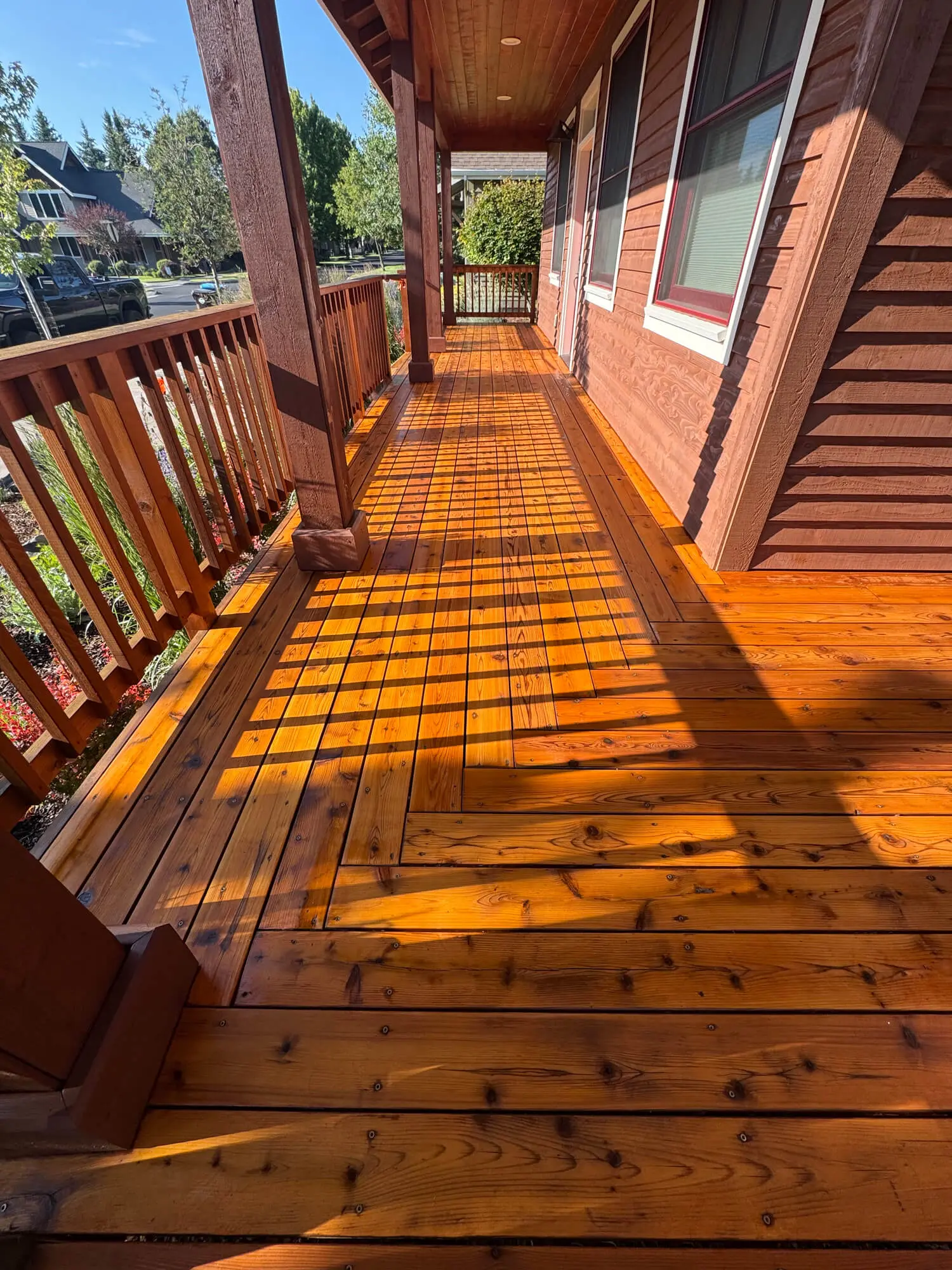 A professional exterior view of a residential backyard featuring a wooden deck with new white vinyl railings and stairs, showcasing a completed project by West Rivers Painting in Bend, OR
