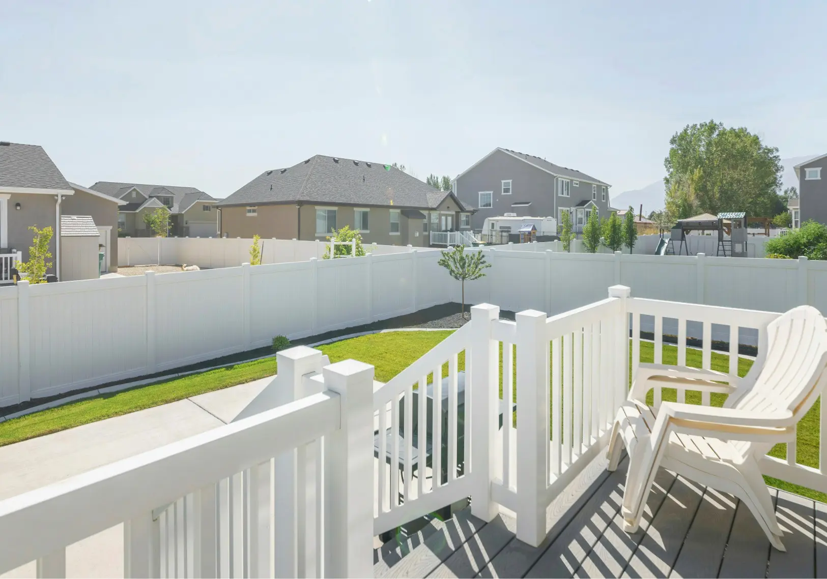 A professional exterior view of a residential backyard featuring a white vinyl fence and a small wooden deck, showcasing a completed project for an article about deck and fence staining services in Bend, OR