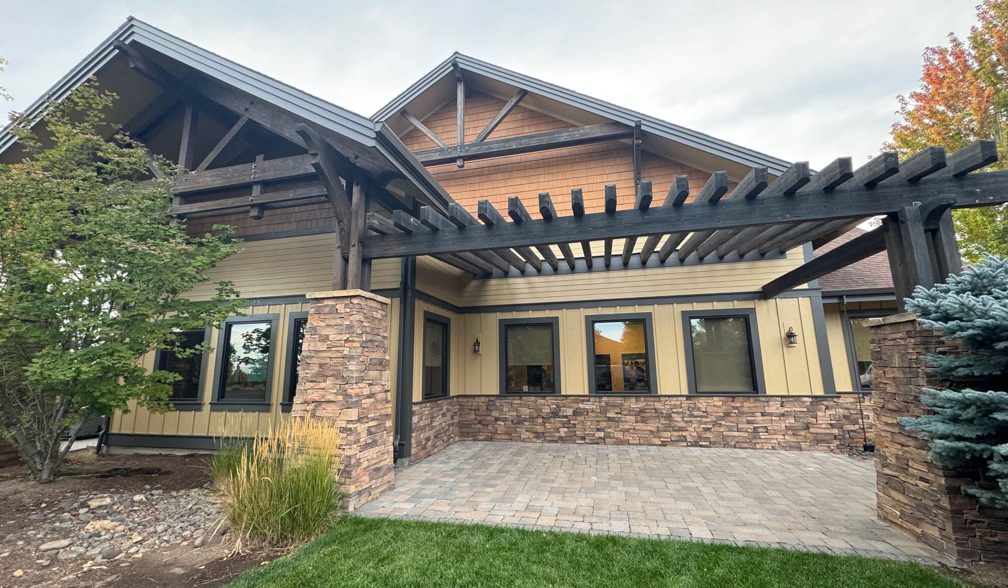 A professionally renovated home exterior featuring a spacious stone-paved patio, elegant timber-framed pergola, and natural stone pillars, creating a sophisticated outdoor living space.
