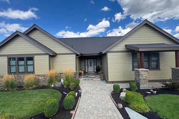 A professionally painted, modern single-story home with neutral siding and stone accents, featuring a well-manicured lawn and a paved walkway leading to the front entrance.