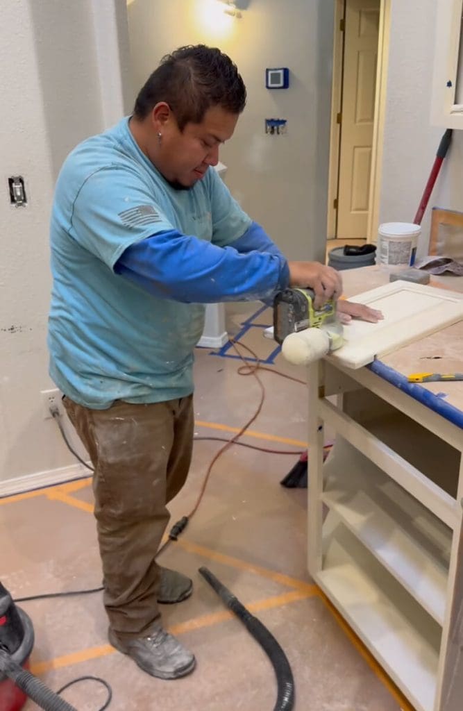 A professional painter from West Rivers Painting carefully sands a wooden cabinet door while working on an interior home renovation project.