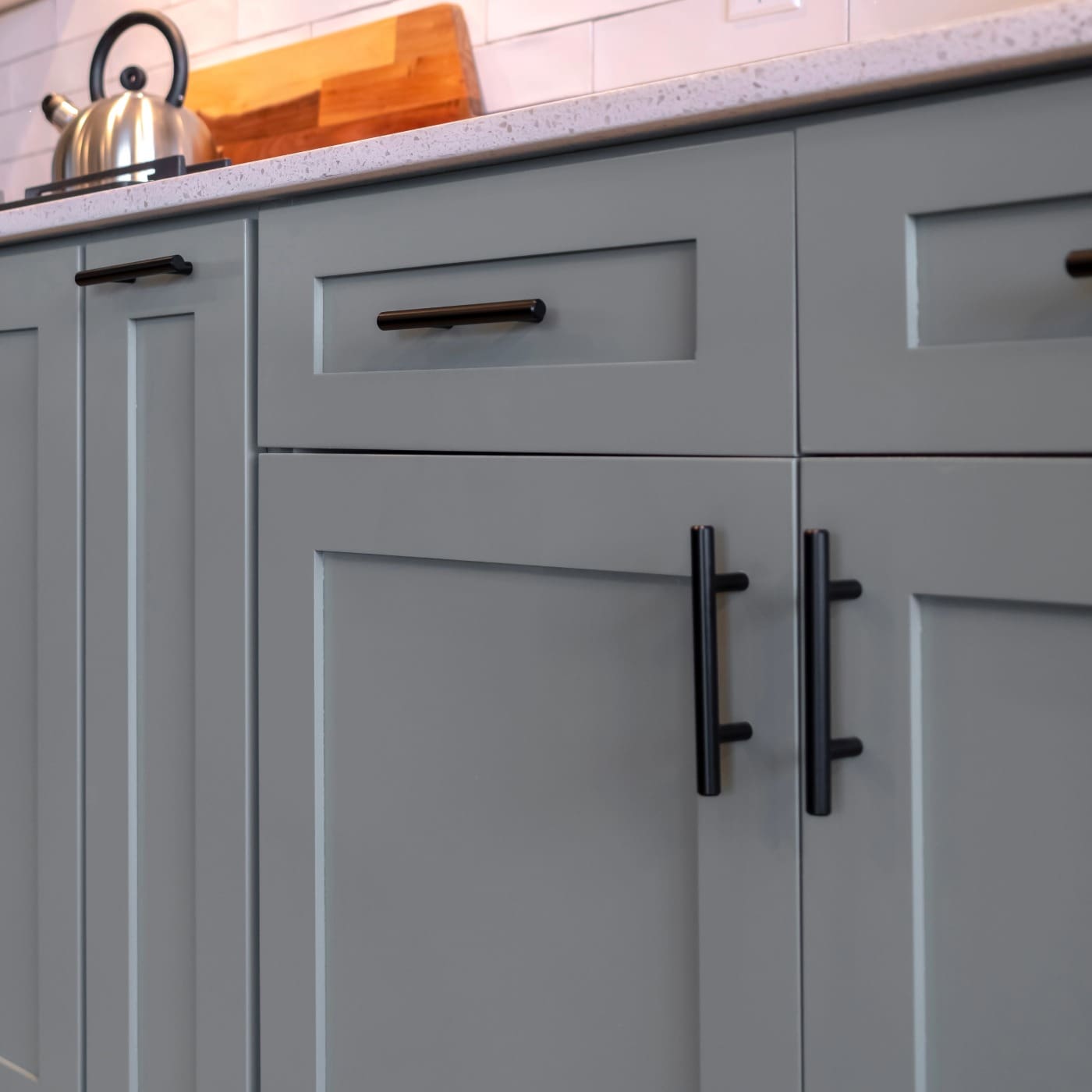A professional interior view of a modern kitchen featuring light gray cabinets with black hardware and white tiled backsplash, showcasing a high-quality finish by West Rivers Painting in Bend, OR.